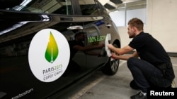 Un empleado instala una calcomanía a un vehículo Nissan Leaf 100% eléctrico cerca del logotipo de la próxima Conferencia sobre Cambio Climático (COP21) en París. Foto de Archivo, Nov. 16 de 2015.