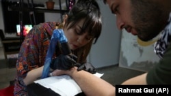 In this Saturday, November 9, 2019, photo, Suraya Shaheedi, 26, Tattoo artist, left, pierced tattoo to a male customer in Kabul, Afghanistan. (AP Photo/Rahmat Gul)