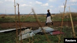 FILE - A mother and child walk past corrugated iron left by residents who intended to build an informal settlement at an open land in Nellmapius township, 20 km (12 miles) east of Pretoria.