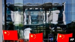 FILE - People display Chinese flags in front of the chancellery which is reflected in the facade of a German parliament building prior to the arrival of Chinese Premier Li Keqiang for a meeting with German Chancellor Angela Merkel in Berlin, July 9, 2018.