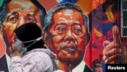 Seorang wanita melewati mural yang menggambarkan Perdana Menteri Malaysia Muhyiddin Yassin di Kuala Lumpur, Malaysia, 27 Oktober 2020. (Foto: REUTERS/Lim Huey Teng)