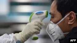 A medical staff member takes the temperature of a man at the Wuhan Red Cross Hospital in Wuhan, Jan. 25, 2020. Wuhan is the city at the center of a spiraling coronavirus outbreak.