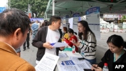 FILE - People look at job listings at a job fair in Chongqing, in southwest China on Nov. 7, 2024.