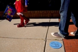 People walk past social-distancing markers meant to help prevent the spread of the new coronavirus as they trick-or-treat for Halloween, Oct. 31, 2020, in downtown Overland Park, Kan.