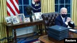 Biden family photos are displayed around a bust of activist Cesar Chavez, as U.S. President Joe Biden prepares to sign executive orders at the Resolute Desk inside the Oval Office of the White House in Washington, U.S., January 20, 2021. Picture taken Jan