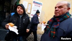 FILE - Needy people eat cheeseburgers donated by McDonald's to a charity organization which bestowed them at a walk-in clinic in Rome, Italy, Jan. 16, 2017. 