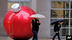 A man and a woman walk in the rain past a holiday ornament, Nov. 29, 2018, in San Francisco. A storm moving into California brought rain that threatened to unleash debris flows in wildfire burn areas.