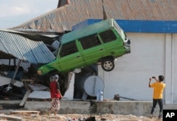 A man takes a photo of a car lifted into the air with his mobile phone following a massive earthquake and tsunami at Talise beach in Palu, Central Sulawesi, Indonesia, Monday, Oct. 1, 2018.