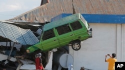 A man takes a photo of a car lifted into the air with his mobile phone following a massive earthquake and tsunami at Talise beach in Palu, Central Sulawesi, Indonesia, Monday, Oct. 1, 2018.