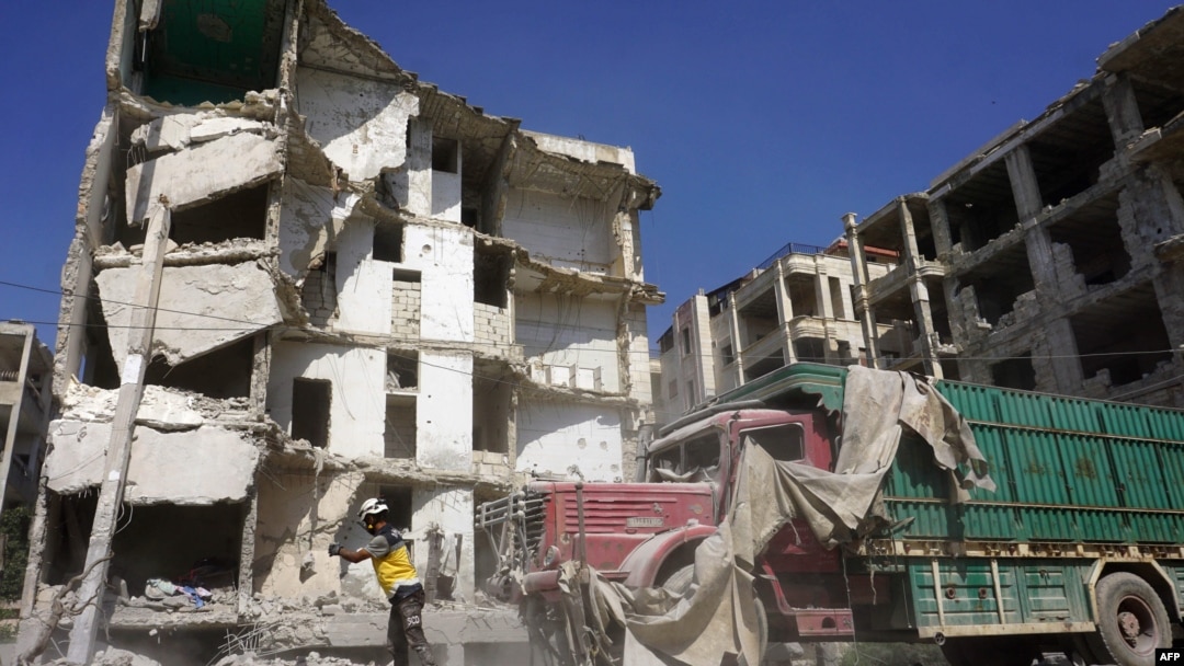 Seorang anggota Pertahanan Sipil Suriah, yg dikenal sebagai Helm Putih, berdiri di depan bangunan yang rusak berat akibat serangan udara oleh pasukan rezim di kota Idlib, 12 Juli 2019. (Foto: dok)