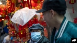 FILE - Karho Leung, 33, right, one of the founders of 12 Pell, a local barbershop, serendipitously happens upon his mother as she sits on a bench along Mott Street in Manhattan's Chinatown neighborhood, Jan. 25, 2024, in New York.