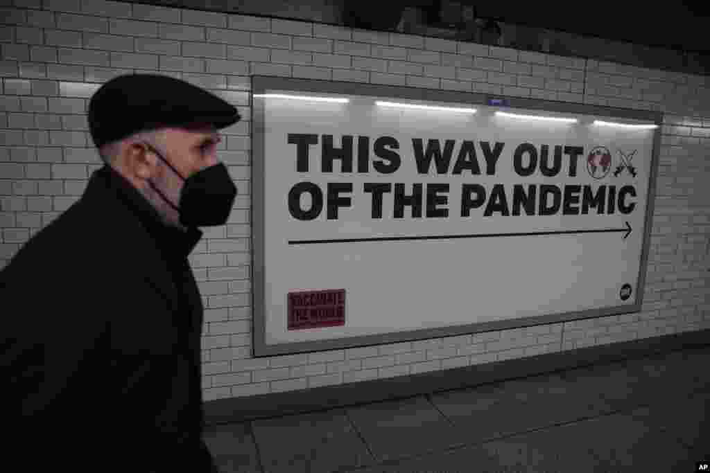 A man wearing a face mask walks past a health campaign poster from the One NGO, in an underpass leading to the Westminster underground train station, in London.