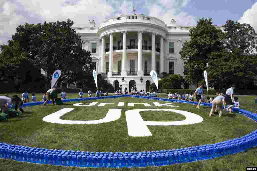 U.S. First Lady Michelle Obama (C) and the Partnership for a Healthier America show a giant &quot;Drink Up&quot; logo, as part of the &quot;Drink Up&quot; campaign aimed at encouraging people to drink more water, on the South Lawn of the White House in Washington, July 22, 2014.