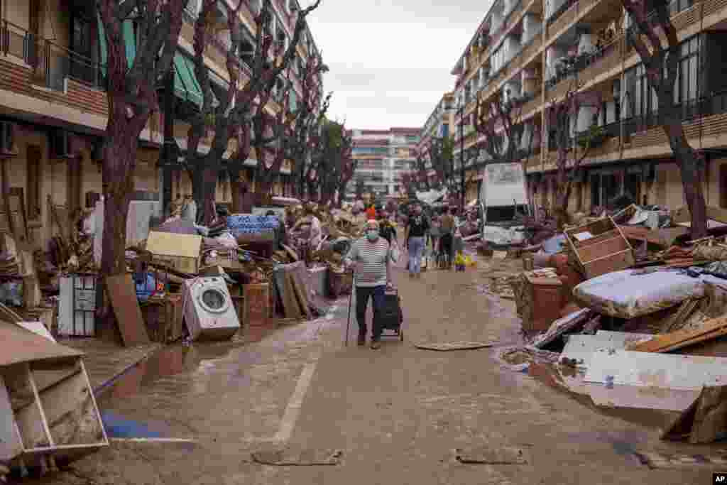 People walk through a street with piled furniture and rubbish on the sides, in an area affected by floods in Benetusser, Spain.