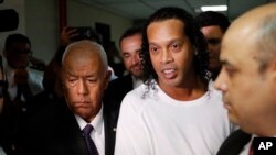 Mantan bintang sepak bola Ronaldinho dikawal polisi menusu pengadilan Justice Palace di Asuncion, Paraguay, Jumat, 6 Maret 2020. (Foto: AP)