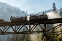 Petugas pemadam kebakaran menyemprotkan air dari kereta api Union Pacific Railroad saat memadamkan Dixie Fire di Hutan Nasional Plumas, California, Jumat, 16 Juli 2021. (AP Photo/Noah Berger)