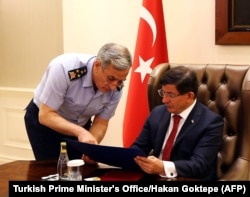 ຜູ້ບັນຊາການກອງທັບອາກາດເທີກີ ພົນເອກ Akin Ozturk (ຊ້າຍ) ແຈ້ງໃຫ້ ນາຍົກລັດຖະມົນຕີເທີກີ ທ່ານ Ahmet Davutoglu ຊາບໂດຍຫຍໍ້ ໃນລະຫວ່າງ ກອງປະຊຸມຄວາມໝັ້ນຄົງພິເສດ ກ່ຽວັກັບລັດອິສລາມ ໃນຊີເຣຍ ແລະ ກຸ່ມ PKK ໃນອີຣັກ, ຢູ່ທີ່ຜະສາດ Cankaya ທີ່ນະຄອນຫຼວງ Ankara ປະເທດເທີກີ, ວັນທີ 25 ກໍລະກົດ 2015.