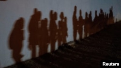 Solicitantes de asilo proyectan sombras en una pared mientras forman una cola para ser procesadas por la Patrulla Fronteriza de EE. UU. después de cruzar el Río Bravo hacia los Estados Unidos desde México en Roma, Texas, el 12 de agosto del 2021.