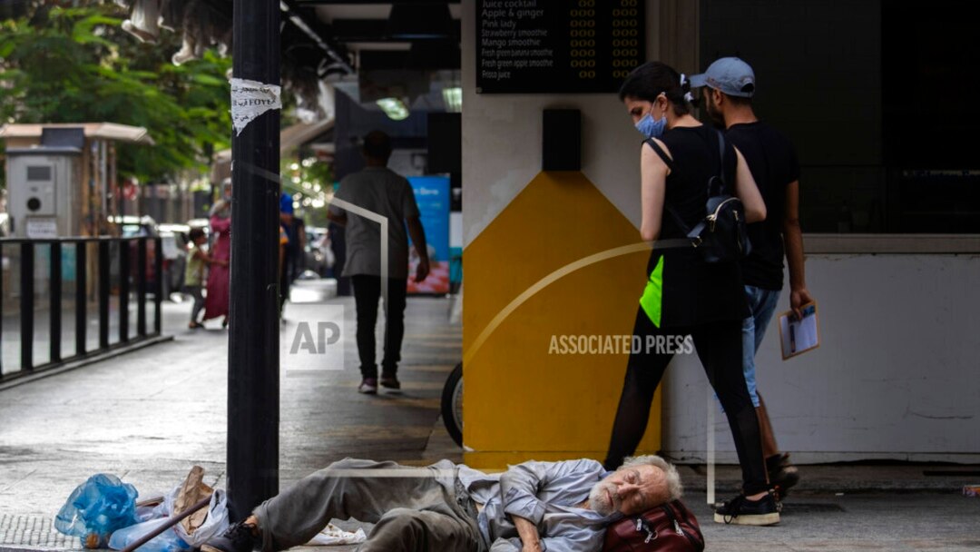 Dalam foto yang diambil pada 17 Juli 2020 ini tampak seorang wanita menatap seorang tuna wisma yang tengah tertidur di area jalan Hamra di kota Beirut, Lebanon. (Foto: AP)