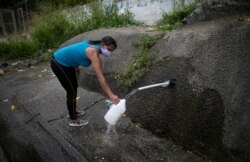 FILE - A woman wearing a face mask to protect against the coronavirus collects water on the side of a road to take home, in Caracas, Venezuela, April 22, 2020.