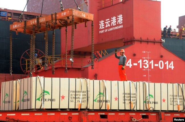 FILE - A worker gestures as a crane lifts goods onto a cargo ship, at a port in Lianyungang, Jiangsu province, China, May 31, 2018.
