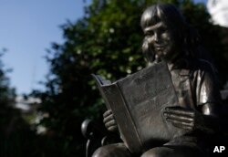 FILE - A young girl statue reads "To Kill a Mockingbird" by author Harper Lee, in Monroeville, Ala., July 13, 2015. Lee passed away Friday morning at age 89.
