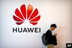 FILE - A man uses his smartphone as he stands near a billboard for Chinese technology firm Huawei at the PT Expo in Beijing, Oct. 31, 2019.