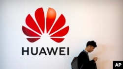 FILE - In this October 31, 2019 photo, a man uses his smartphone as he stands near a billboard for Chinese technology firm Huawei at PT Expo in Beijing.