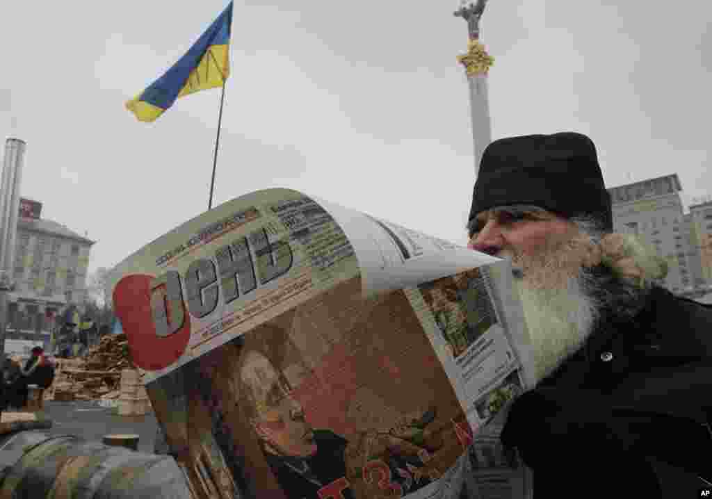 A man reads a newspaper with a picture of Russian President Vladimir Putin on the front page during a pro-European Union rally in Independence Square, Kyiv, Ukraine, Dec. 19, 2013.