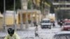 A Cambodian motorcyclist maneuvers through a flooded street along side cars on a rainy day in Phnom Penh.