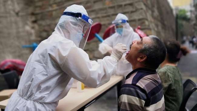 在中国新疆乌鲁木齐一名穿着防护服的医务工作者对居民进行核酸检测。（2020年7月19日）