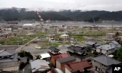 FILE - Undamaged homes are seen on a hillside in the foreground as a tsunami-damaged area is seen behind in the town of Ofunato, in northeast Japan, Sept. 5, 2011.