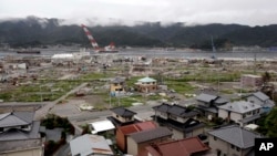 FILE - Undamaged homes are seen on a hillside in the foreground as a tsunami damaged area is seen behind in the town of Ofunato, in northeast Japan, Monday, Sept. 5, 2011.