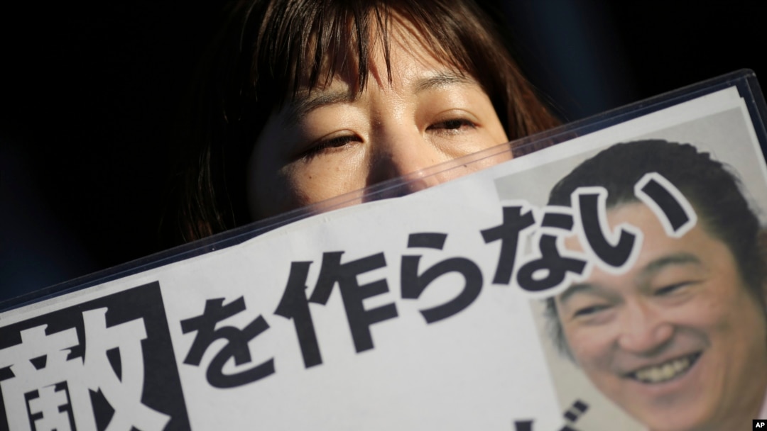 Seorang perempuan memegang poster bertuliskan: "Jangan mencari musuh" dan membawa fotonya di depan kediaman resmi perdana menteri di Tokyo, 1 Februari 2015.
