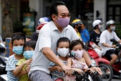 A man and his children, all wearing protective masks, ride a bicycle on a street during the coronavirus outbreak, in Hanoi, Vietnam, July 27, 2020.