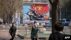 FILE - People wearing face masks walk before a propaganda poster displayed on a street in Pyongyang, April 9, 2020. 