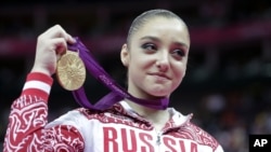 Russian gymnast Aliya Mustafina displays the gold medal for her performance on the uneven bars during the artistic gymnastics women's apparatus finals at the 2012 Summer Olympics, Aug. 6, 2012, in London. 