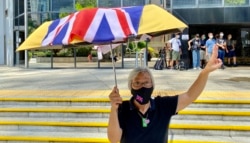 社运人士王婆婆9月15日在湾仔区域法院外撑起贴上英国国旗的黄伞，声援六四未经批准集结案，12名认罪的被告（美国之音/汤惠芸）