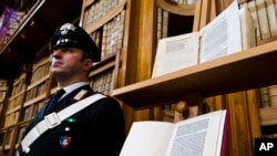 A Carabinieri policeman stands May 18, 2016, next to a book, bottom, reproducing a letter written by Christopher Columbus in 1493 about his discovery of the New World that had been replaced at Florence's Riccardiana library with a forgery, at top, that no one noticed until a few years ago, during a press conference in Rome. 