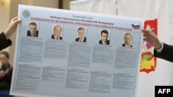 Russian election officials hold an election poster showing the candidates.
