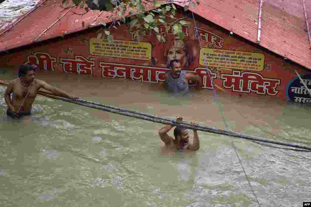 People wade through outside a submerged Hanuman temple as the water levels of the Ganges and Yamuna rivers rise in Allahabad, India, Aug. 7, 2021.