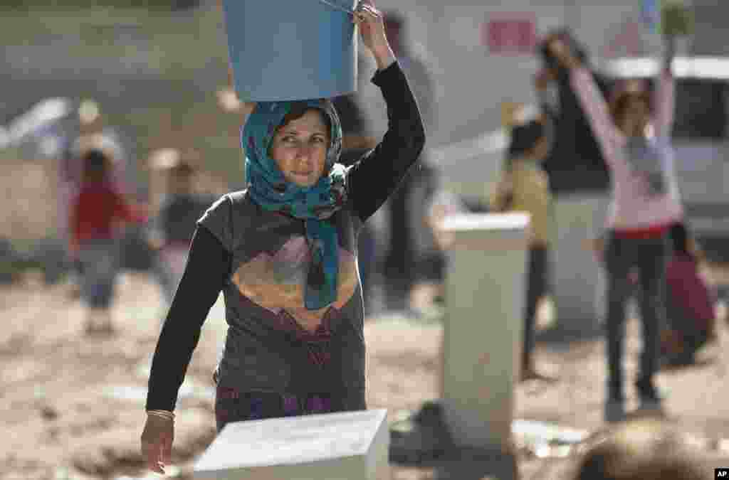 Une femme de réfugié kurde syrienne de la région Kobané porte un seau d&#39;eau sur la tête dans un camp de Suruc, près de la frontière Turquie-Syrie lundi 3 novembre 2014.