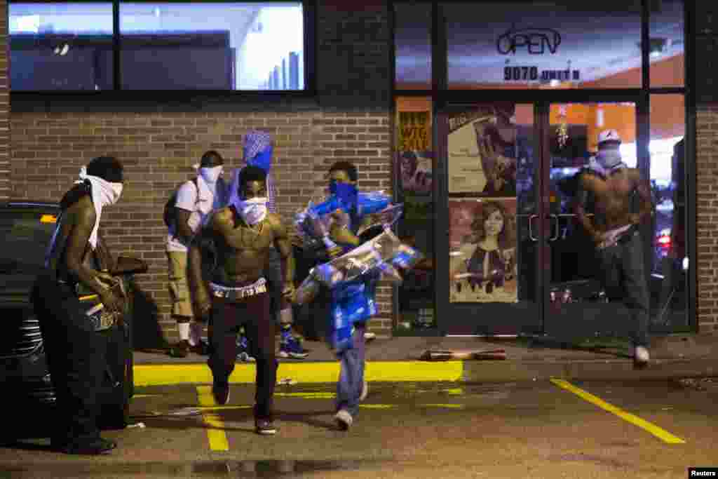 Masked individuals carry items out of a store in Ferguson, Aug. 16, 2014.