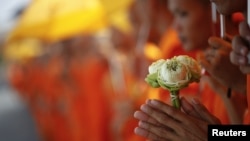 A Buddhist monk holds flowers as he joins others waiting for the coffin of the former king Norodom Sihanouk to arrive at the Royal Palace in Phnom Penh October 17, 2012. Tens of thousands poured into Cambodia's capital to witness the procession on Wednesday. 