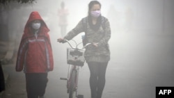 FILE - A woman walks with her child on a street as schools were closed due to the heavy smog in Jilin, northeast China's Jilin province. 