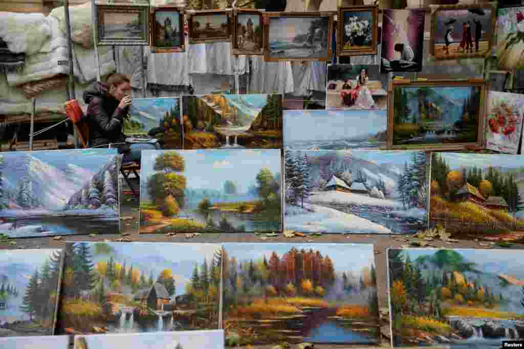 A street vendor selling paintings drinks hot tea while waiting for customers on a sidewalk in central Lviv, Ukraine. 