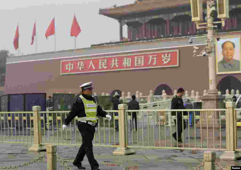 A police officer walks in front of the giant portrait of the late Chinese Chairman Mao Zedong as other police clean up after a car crash at Tiananmen Square in Beijing, Oct. 28, 2013. 