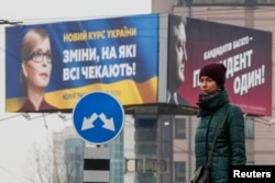A woman stands in front of pre-election posters of opposition politician Yulia Tymoshenko and Ukrainian President Petro Poroshenko in Kyiv, Ukraine, Feb. 20, 2019.