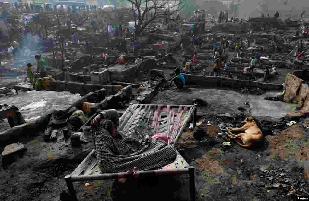 A woman sits on a broken bed with her family dog on the floor of a burnt-out house as people search for their belongings after a fire broke out in a slum in Karachi, Pakistan, Jan. 22, 2020.