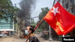 FILE - A man holds a National League for Democracy (NLD) flag during a protest against the military coup, in Yangon, Myanmar March 27, 2021. 